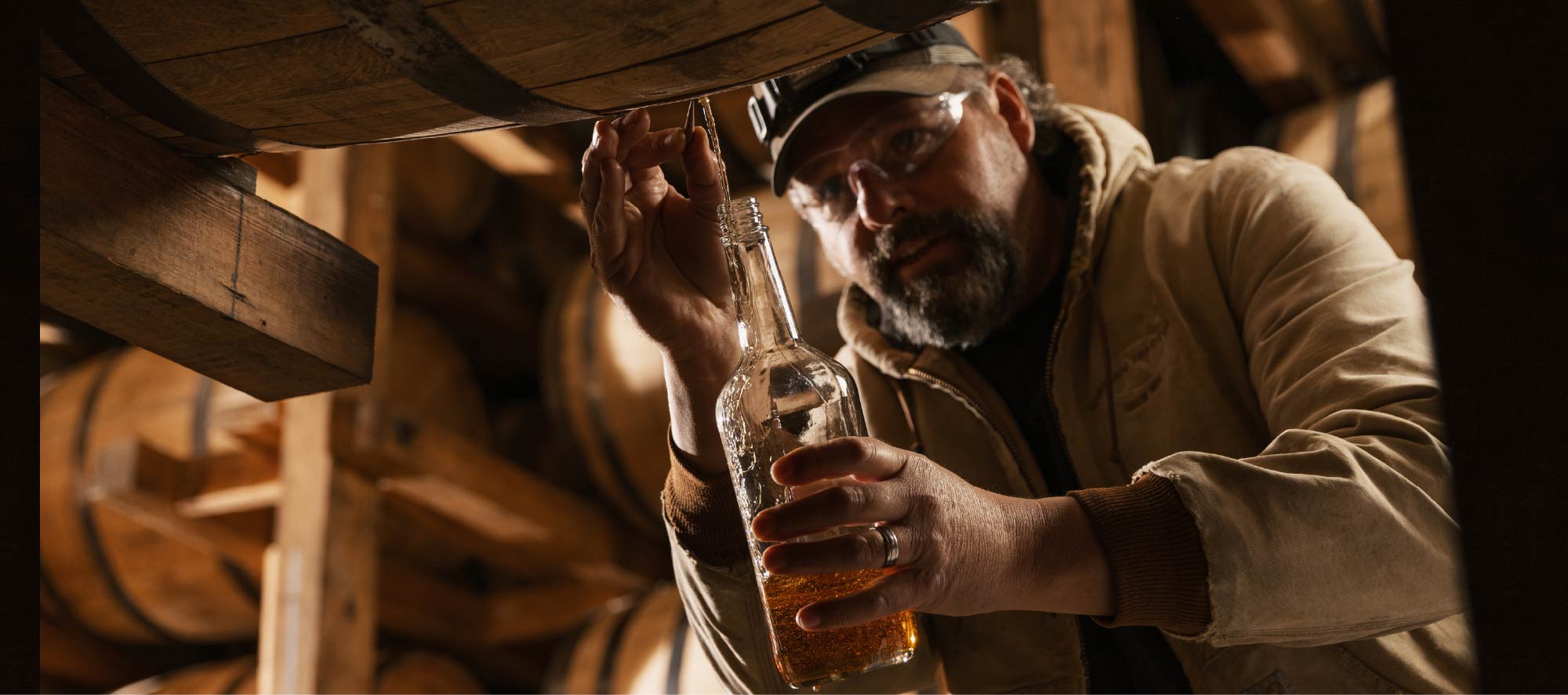 A man pours bourbon straight from the barrel into a clear bottle