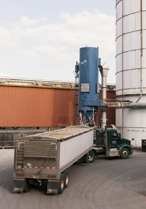 A large truck pulls up to a factory silo