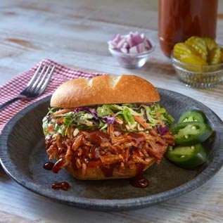 A BBQ sandwich with coleslaw and jalapeño peppers on a black plate